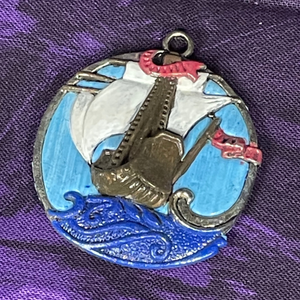 A painted metal pendant of a white mast sailing ship.